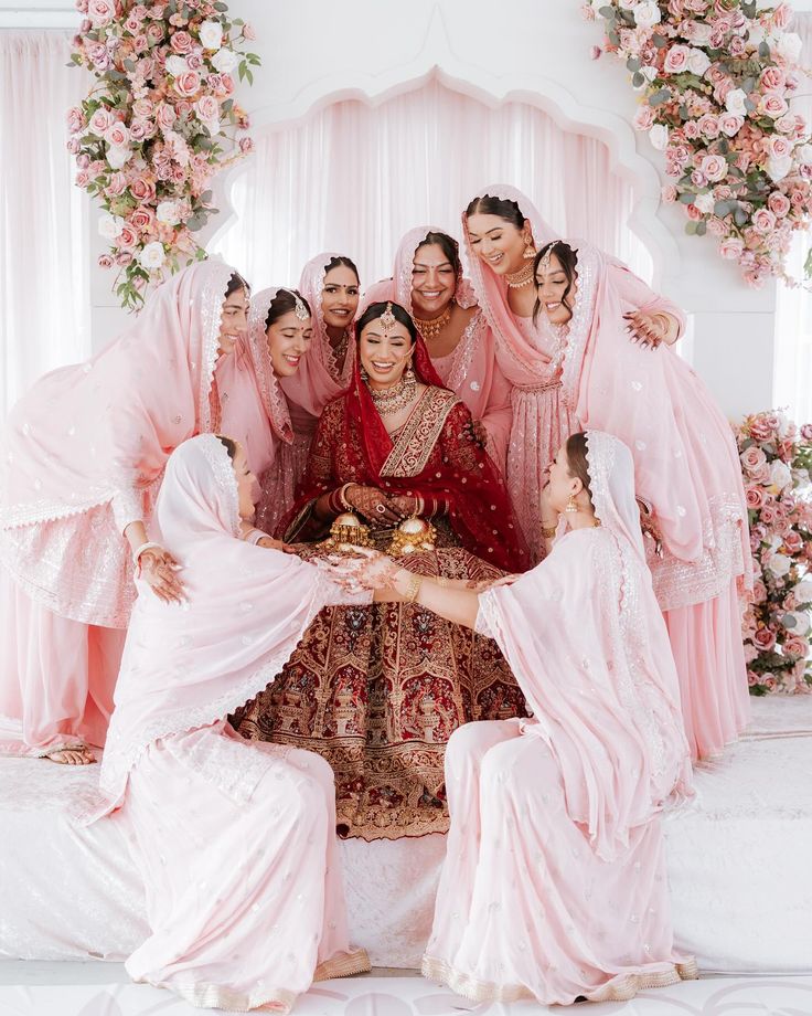 A bride in a red lehenga surrounded by her closest women in blush pink