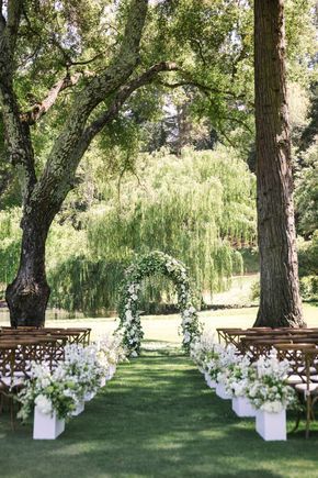A garden ceremony under old trees with a white floral arch