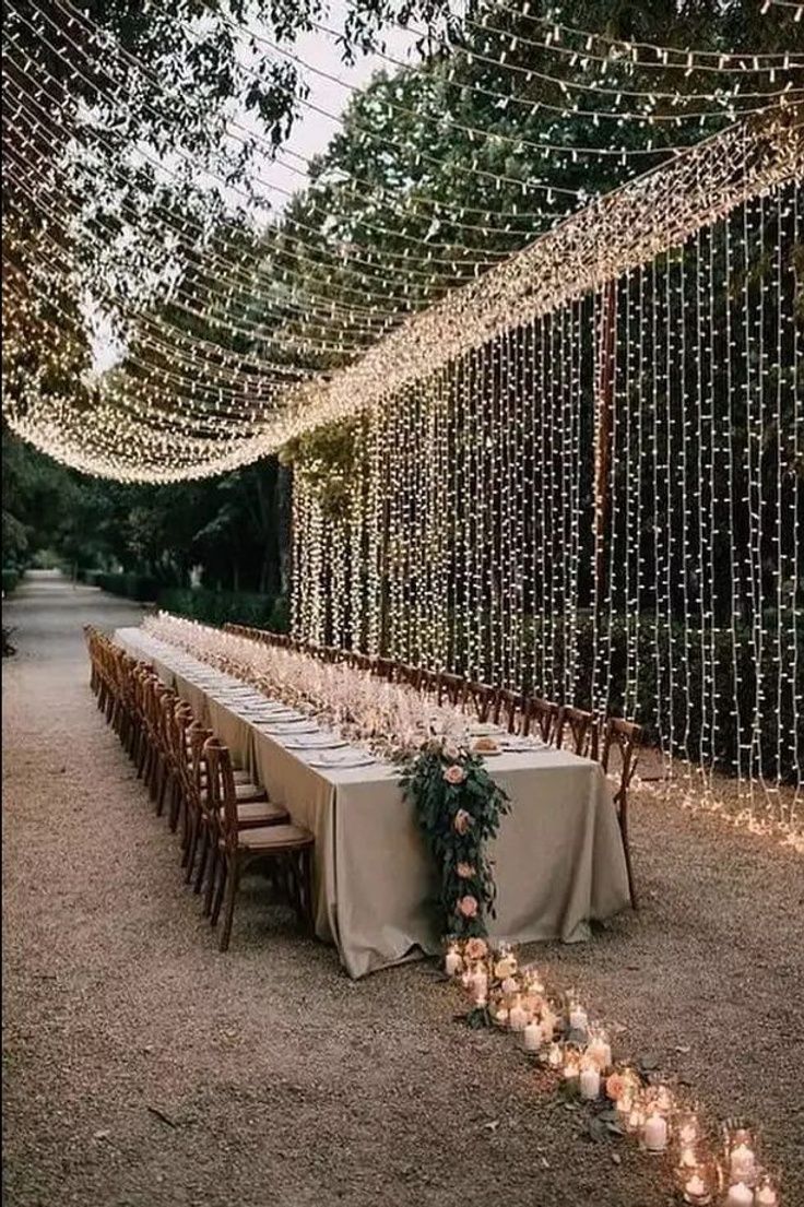 One long candlelit dinner table under a canopy of string lights